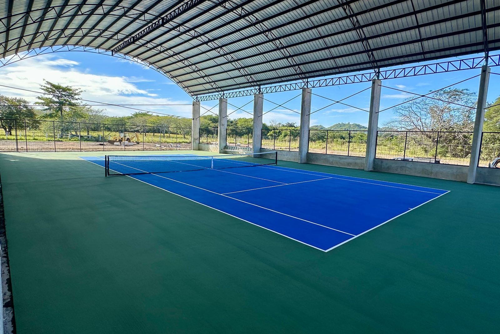 The covered court pavilion at Finca Escondida, blue courts and green frame with open sides to the fields